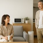 50代の日本人夫婦が明るいリビングでくつろぎながら、空気清浄機や電子レンジなど生活家電に囲まれて快適に過ごしている様子